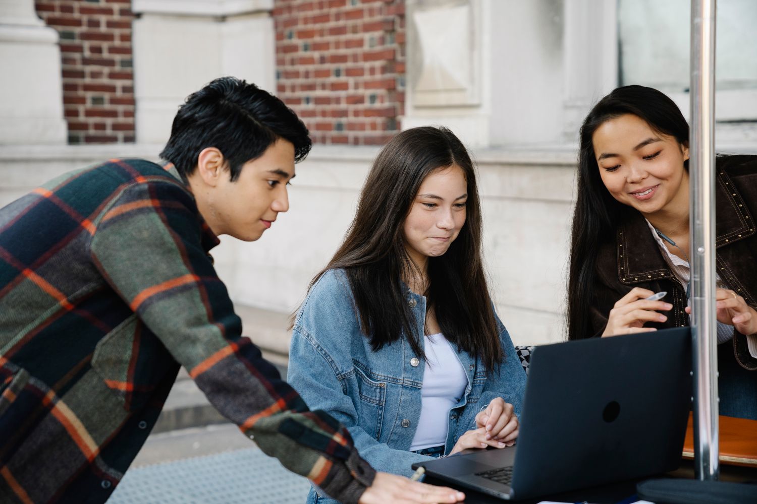 University students collaborating on a laptop outside a campus building